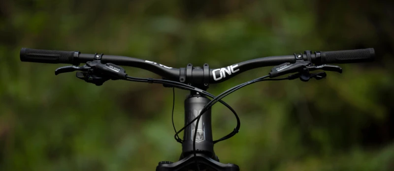 Detalle frontal del manillar OneUp Carbon montado en bicicleta de mountain bike mostrando el logotipo de la marca